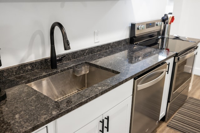 kitchen with stainless steel appliances, a sink, white cabinets, light wood-style flooring, and dark stone counters