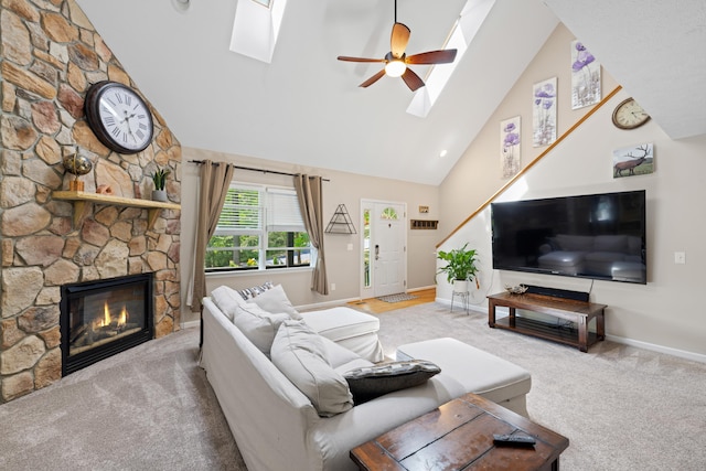 carpeted living area with a skylight, high vaulted ceiling, baseboards, a stone fireplace, and a ceiling fan