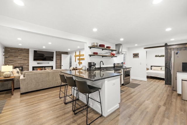 kitchen with stainless steel appliances, a barn door, a breakfast bar, light wood-style flooring, and open shelves