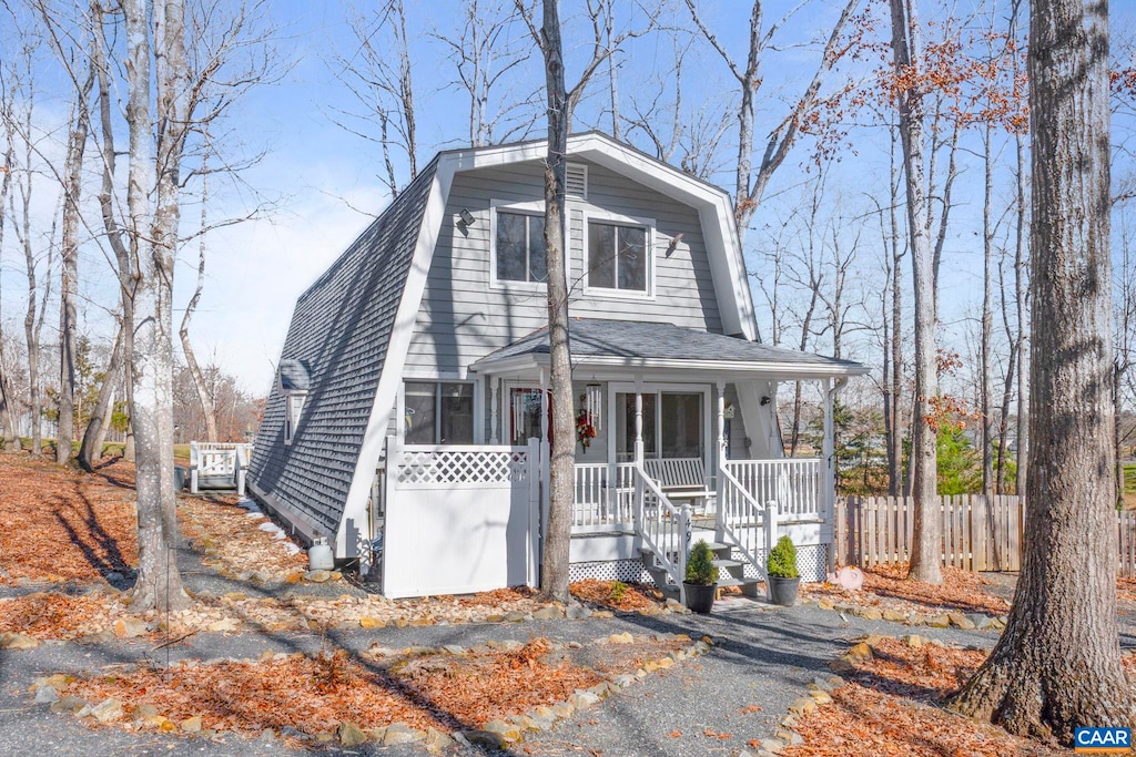 view of front of home with covered porch, fence, a shingled roof, and a gambrel roof