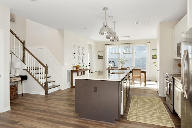 kitchen with a kitchen island with sink, dark wood finished floors, a sink, light countertops, and stainless steel appliances