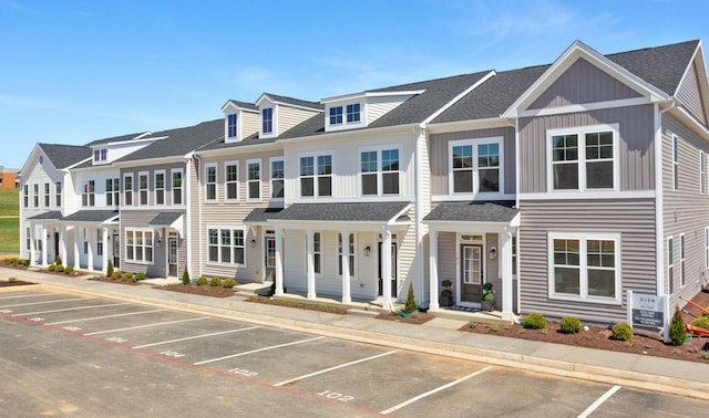 townhome / multi-family property with covered porch, a shingled roof, and uncovered parking