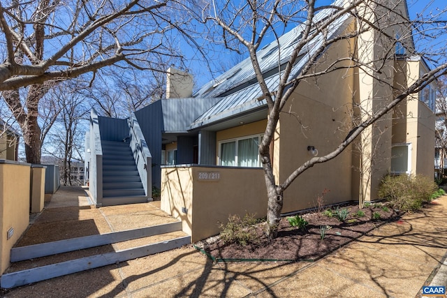 view of front of house with fence, stucco siding, stairway, metal roof, and a chimney