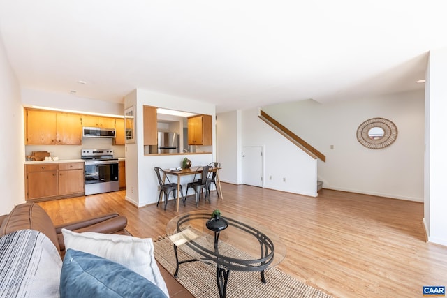 living area with stairway, light wood-style flooring, and baseboards
