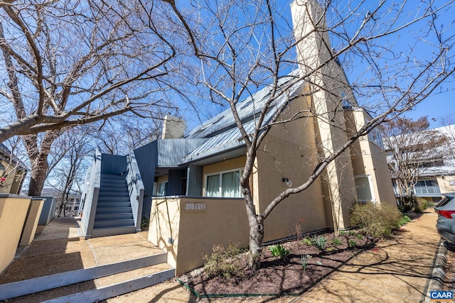 view of front of home with metal roof, stairs, and a chimney