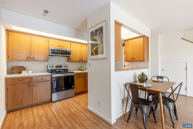 kitchen with light wood-type flooring, baseboards, light countertops, and appliances with stainless steel finishes