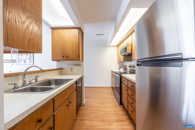 kitchen featuring light wood finished floors, light countertops, stainless steel appliances, and a sink