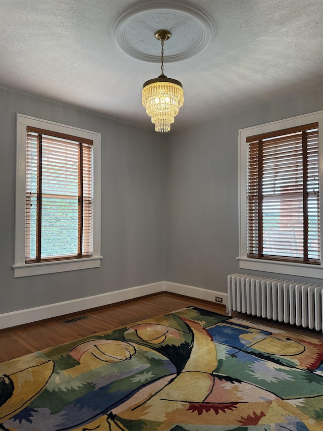228 Hendren Ave, Staunton, VA 24401 - empty room with radiator heating unit, a chandelier, wood finished floors, plenty of natural light, and a textured ceiling