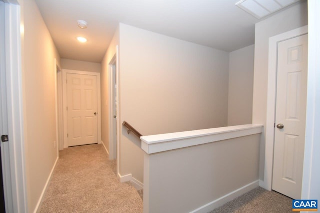 hall featuring an upstairs landing, baseboards, and light colored carpet