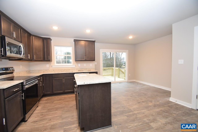 kitchen featuring appliances with stainless steel finishes, light wood-style floors, a kitchen island, and light stone countertops