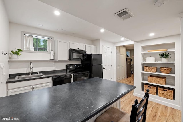  - kitchen featuring black appliances, a sink, dark countertops, open shelves, and light wood-type flooring