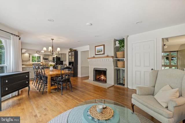  - living room featuring plenty of natural light, a chandelier, light wood-style floors, and a brick fireplace