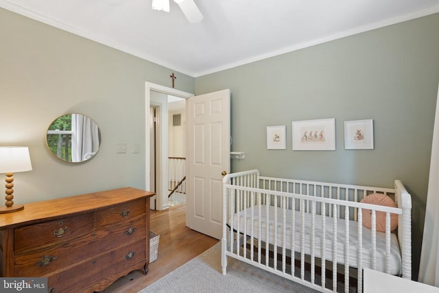  - bedroom featuring wood finished floors, ornamental molding, ceiling fan, and a nursery area