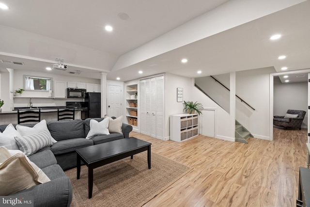  - living area featuring light wood-type flooring, recessed lighting, stairs, decorative columns, and baseboards