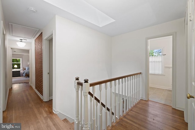  - corridor with an upstairs landing, attic access, wood finished floors, and a skylight