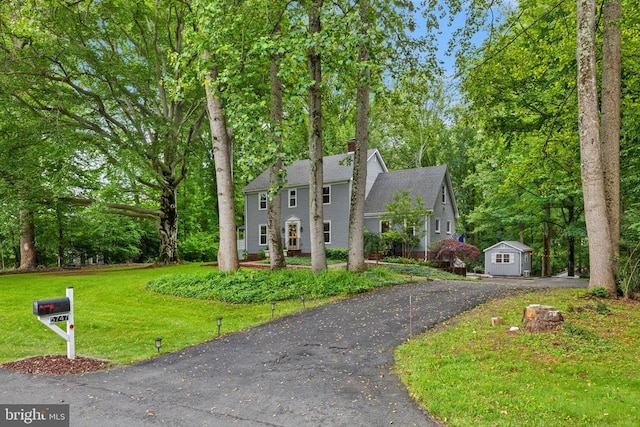  - colonial inspired home featuring a front yard, a chimney, and driveway
