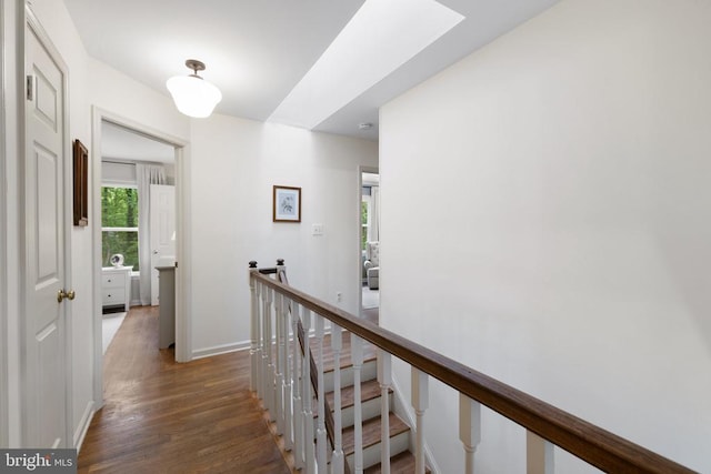  - hall with an upstairs landing, wood finished floors, baseboards, and a skylight
