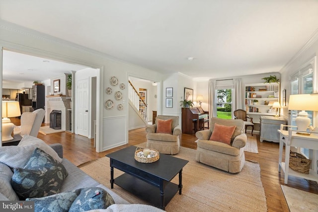  - living area featuring stairway, wood finished floors, crown molding, a fireplace with flush hearth, and wainscoting