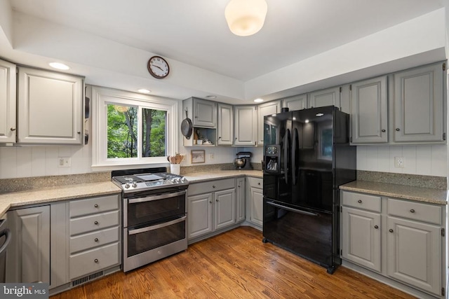  - kitchen featuring black fridge, double oven range, gray cabinetry, wood finished floors, and light countertops