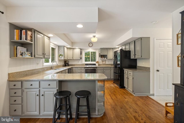  - kitchen with gray cabinetry, stainless steel appliances, a peninsula, a sink, and wood finished floors