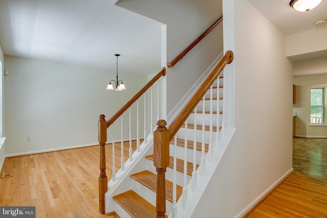  - staircase with wood finished floors, baseboards, and a chandelier