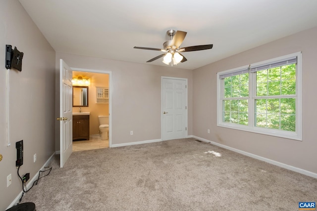 unfurnished bedroom featuring light colored carpet, baseboards, connected bathroom, and ceiling fan