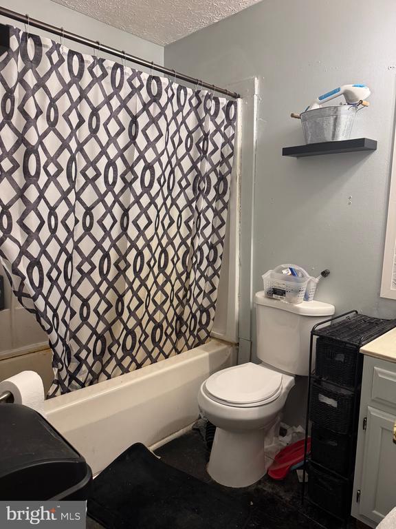 bathroom with a textured ceiling, shower / tub combo with curtain, toilet, and vanity