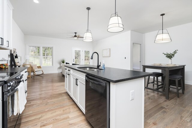 kitchen featuring dishwasher, white cabinetry, range with electric cooktop, an island with sink, and decorative light fixtures