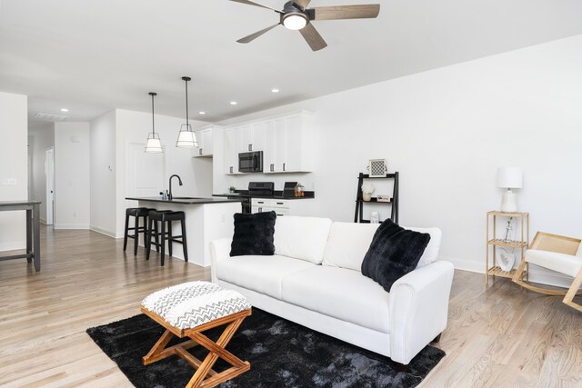 living room featuring sink, ceiling fan, and light wood-type flooring