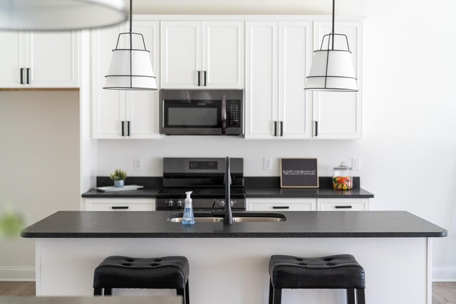 kitchen with white cabinetry, a kitchen island with sink, pendant lighting, and electric stove