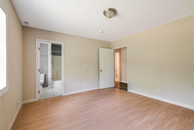 unfurnished bedroom with light wood finished floors, baseboards, a textured ceiling, and ensuite bath
