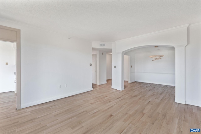 unfurnished room featuring arched walkways, light wood-style floors, a textured ceiling, ornamental molding, and baseboards