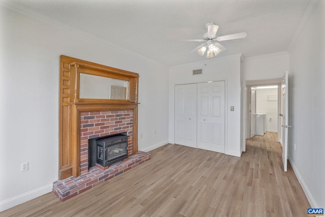 unfurnished living room featuring a wood stove, light wood finished floors, crown molding, a ceiling fan, and baseboards