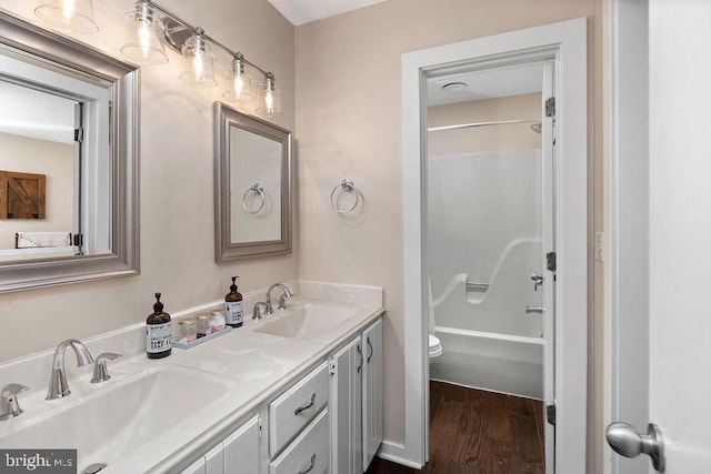 bathroom featuring double vanity, toilet, a sink, and wood finished floors