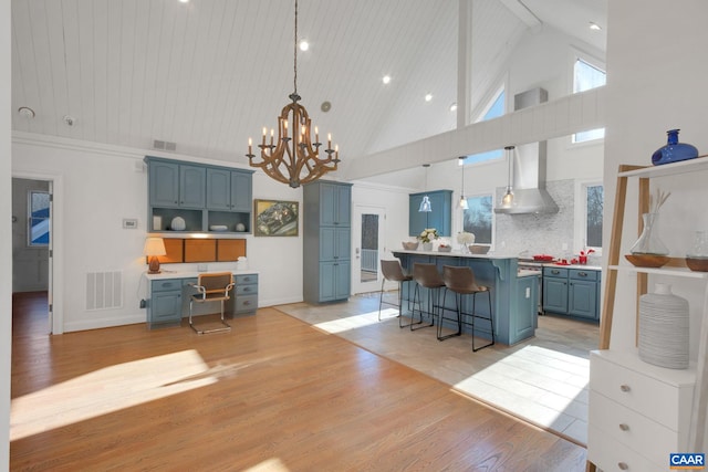 kitchen featuring a breakfast bar area, high vaulted ceiling, visible vents, wall chimney range hood, and blue cabinetry