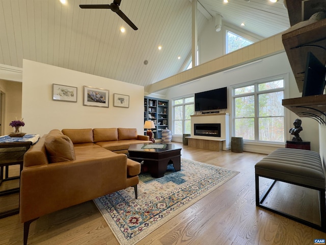 living area featuring a glass covered fireplace, ceiling fan, wood ceiling, high vaulted ceiling, and wood finished floors