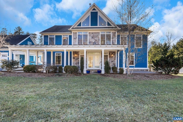 view of front of property featuring covered porch, stone siding, and a front lawn