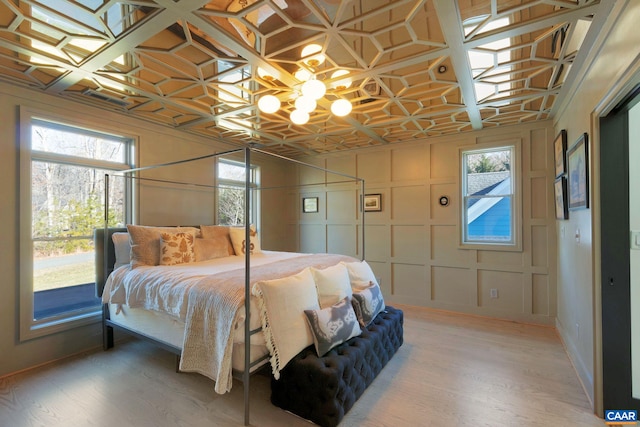 bedroom featuring light wood finished floors, a decorative wall, an ornate ceiling, and an inviting chandelier