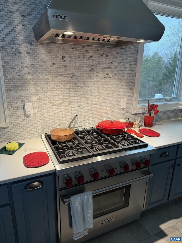 kitchen featuring under cabinet range hood, stainless steel range, tile patterned floors, decorative backsplash, and light countertops