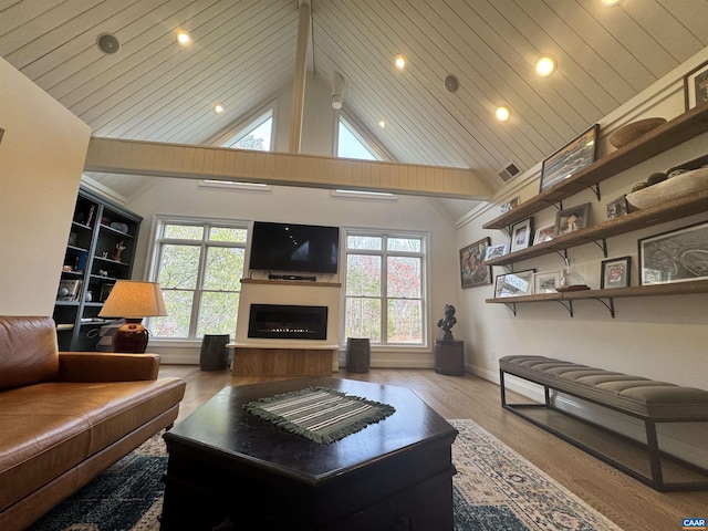 living room featuring wood finished floors, high vaulted ceiling, a fireplace with raised hearth, visible vents, and baseboards
