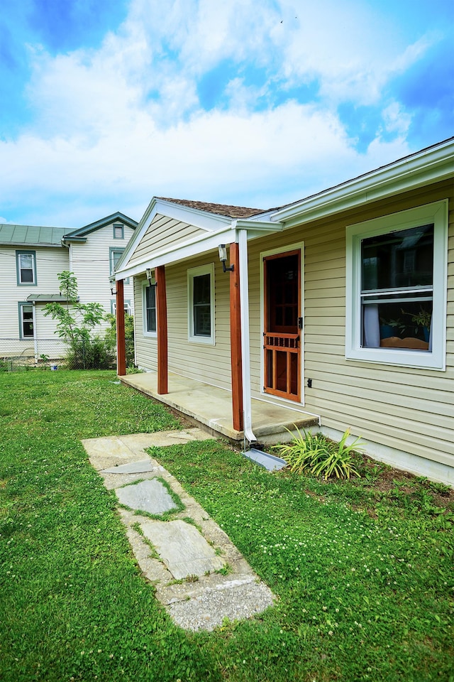 view of exterior entry featuring a lawn and covered porch