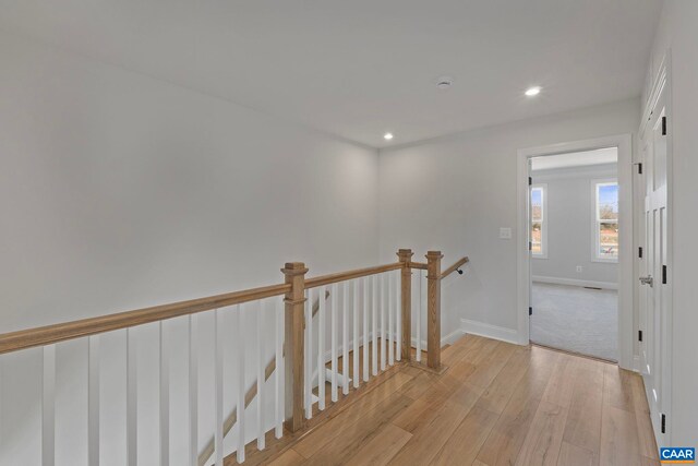 corridor featuring light wood finished floors, baseboards, an upstairs landing, and recessed lighting