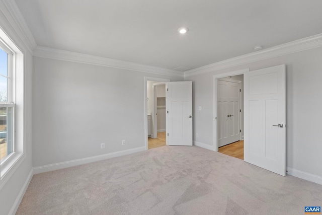 unfurnished bedroom featuring a spacious closet, light carpet, baseboards, and ornamental molding