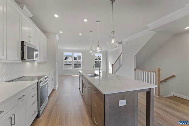 kitchen featuring a sink, stainless steel appliances, a kitchen island with sink, crown molding, and baseboards