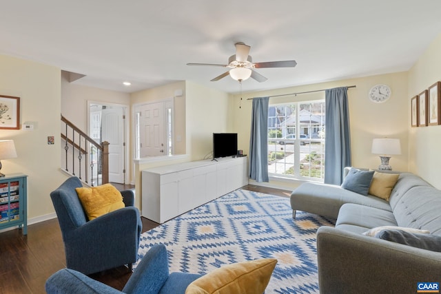 living area with wood finished floors, a ceiling fan, stairs, and baseboards