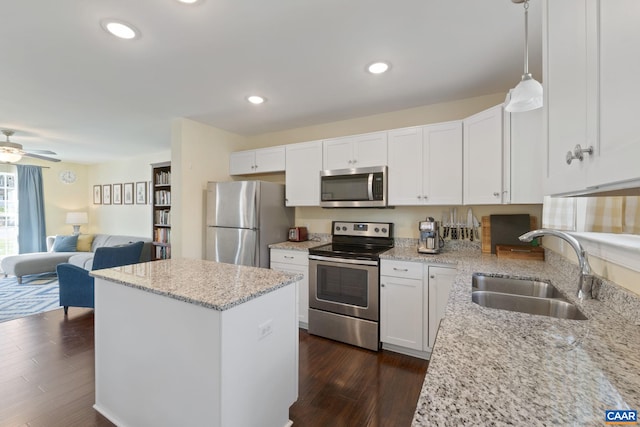 kitchen with stainless steel appliances, a sink, open floor plan, a center island, and dark wood-style floors