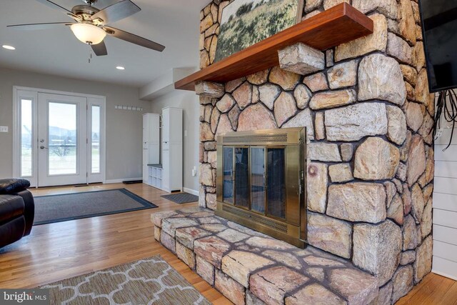living area featuring wood finished floors, a stone fireplace, ceiling fan, and recessed lighting