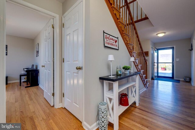 hallway featuring light wood finished floors, stairway, and baseboards