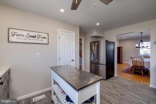 kitchen with stainless steel refrigerator with ice dispenser, ceiling fan, wood finished floors, baseboards, and a chandelier