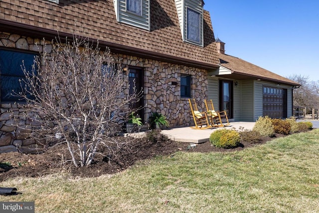 rear view of property featuring stone siding, roof with shingles, a garage, and a yard